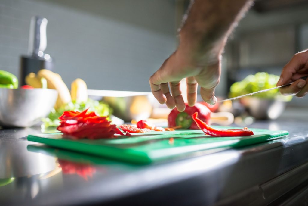 Mains découpant des légumes frais sur une planche en bois